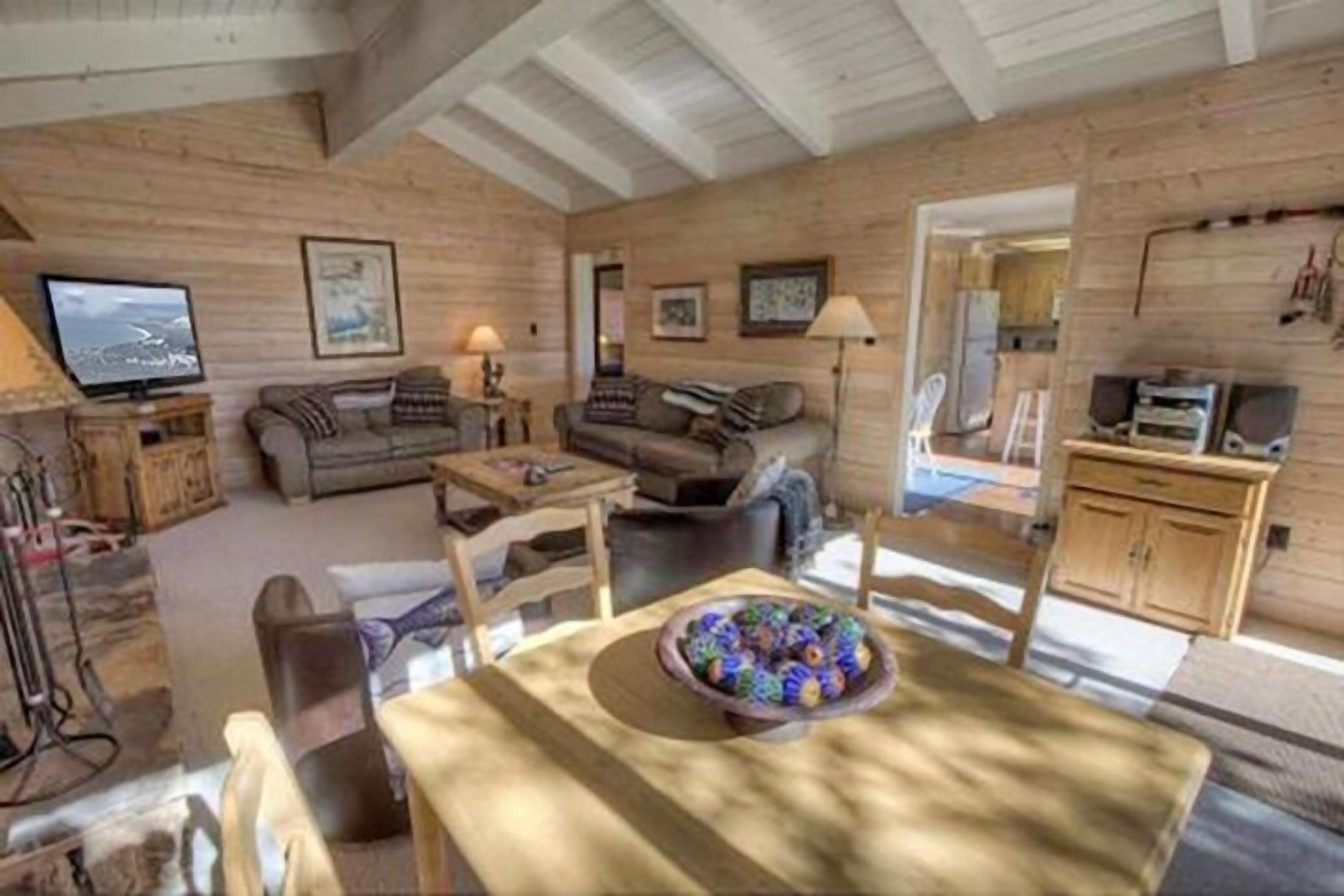 L’intérieur chaleureux d’un chalet, avec un décor en bois, un coin repas agrémenté d’un panier de fruits et un téléviseur dans le salon.