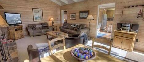 Interior acogedor de una cabaña con detalles de madera, un comedor con un frutero y un televisor en la sala.