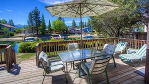Una terraza con una mesa y sillas de vidrio, con vista a un lago y un paisaje montañoso.