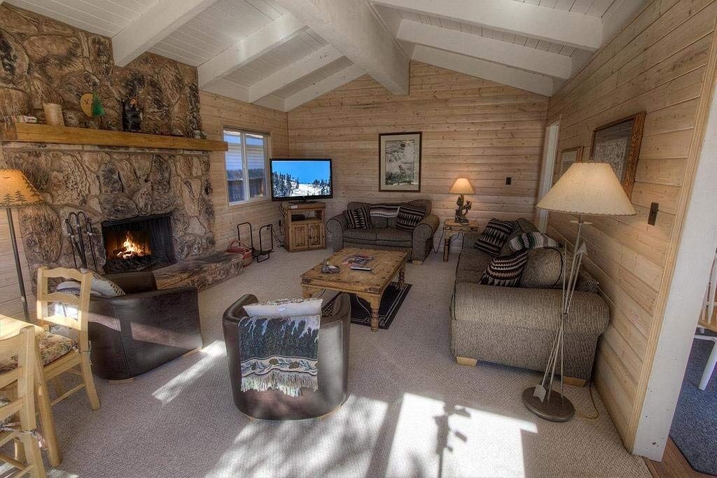 A cozy log cabin interior with a stone fireplace, wooden walls, a television, and comfortable seating.