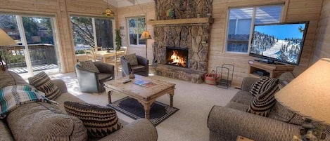 A cozy cabin interior with a stone fireplace, wooden furniture, and a television.