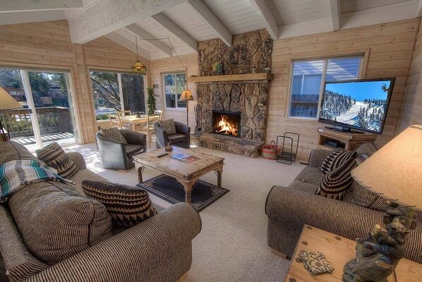 A cozy cabin interior with a stone fireplace, wooden furniture, and a television. - 2186 Morro Drive 3 Bedroom Home (South Lake Tahoe)