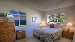 Un dormitorio con una cama, dos mesitas de noche con lámparas, un aparador, un ventanal con vistas y un cuadro en la pared.