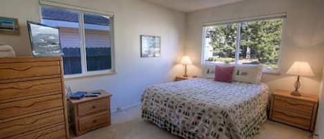 Un dormitorio con una cama, dos mesitas de noche con lámparas, un aparador, un ventanal con vistas y un cuadro en la pared.