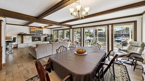 A spacious living room with a fireplace, a dining area with a table and chairs, and a view of a lake with boats. - 2148 Inverness Drive 3 Bedroom Home (South Lake Tahoe)