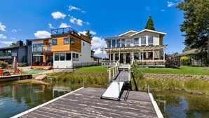 A modern house with a dock leading to a water body, surrounded by greenery and clear skies. - 2148 Inverness Drive 3 Bedroom Home (South Lake Tahoe)