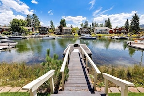 Un muelle de madera que conduce a un lago tranquilo con barcos, rodeado de casas residenciales.