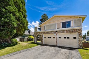 Une maison à deux étages avec une façade en pierre, un garage à deux portes et un grand arbre dans le jardin.