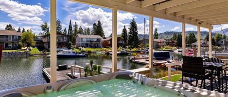 A hot tub with a view of a lake and boats, surrounded by a covered patio with chairs and tables.