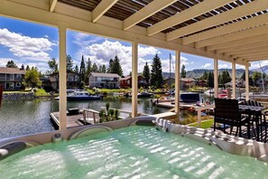 Un bain à remous avec vue sur un lac et des bateaux, entouré d’une terrasse couverte avec des chaises et des tables.