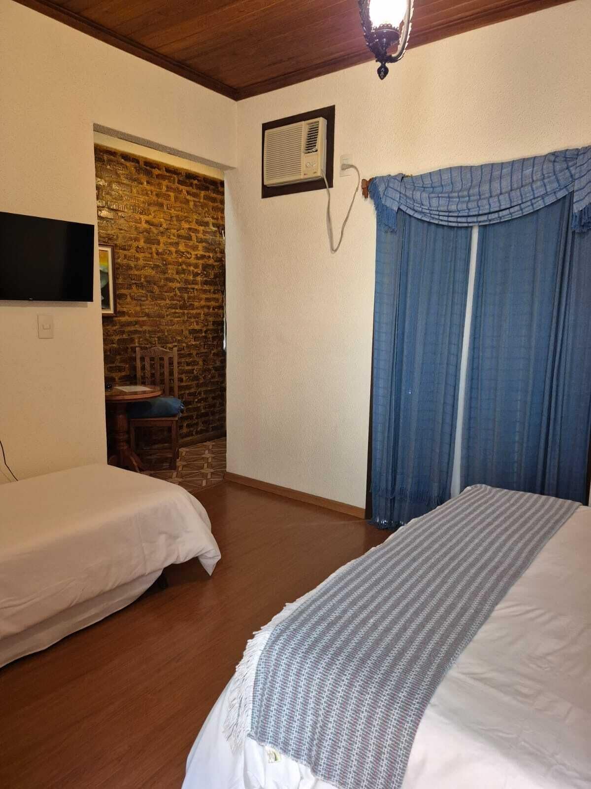 A room with two beds, a brick wall, a television, and a window with curtains.