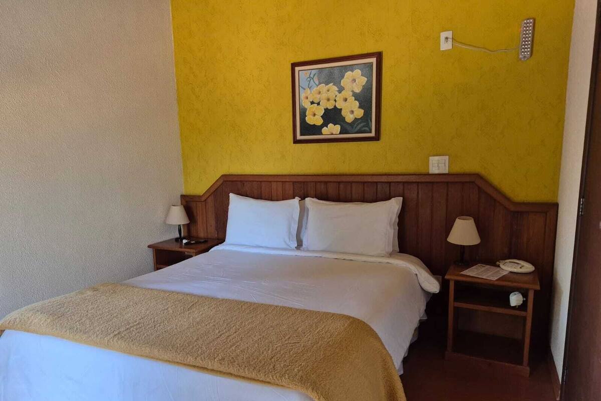 Ein Hotelzimmer mit einem Bett, zwei Nachttischen, einer Lampe, einem Telefon und einem an der Wand befestigten Lichtschalter.
