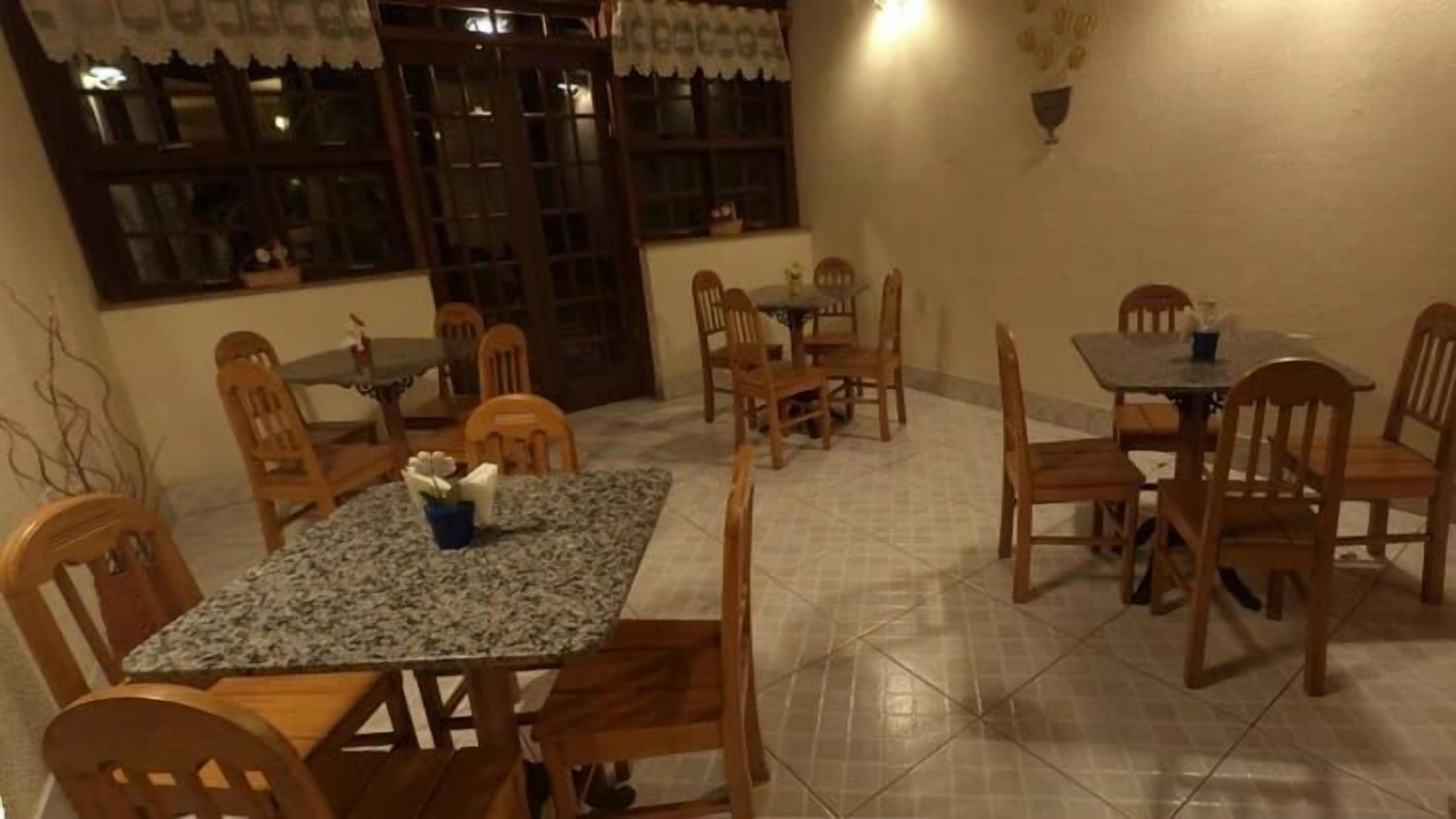 Uma área de refeições com uma mesa retangular, várias cadeiras de madeira e piso ladrilhado.