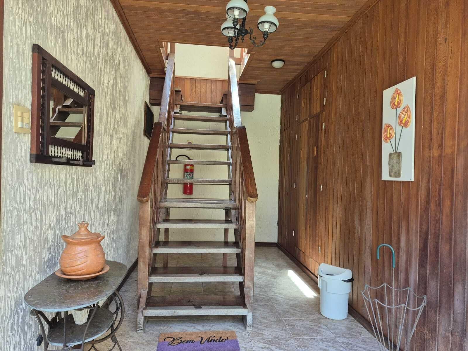 A wooden staircase leading to an upper floor, a small table with a clay pot, a trash bin, and a wall-mounted light fixture.