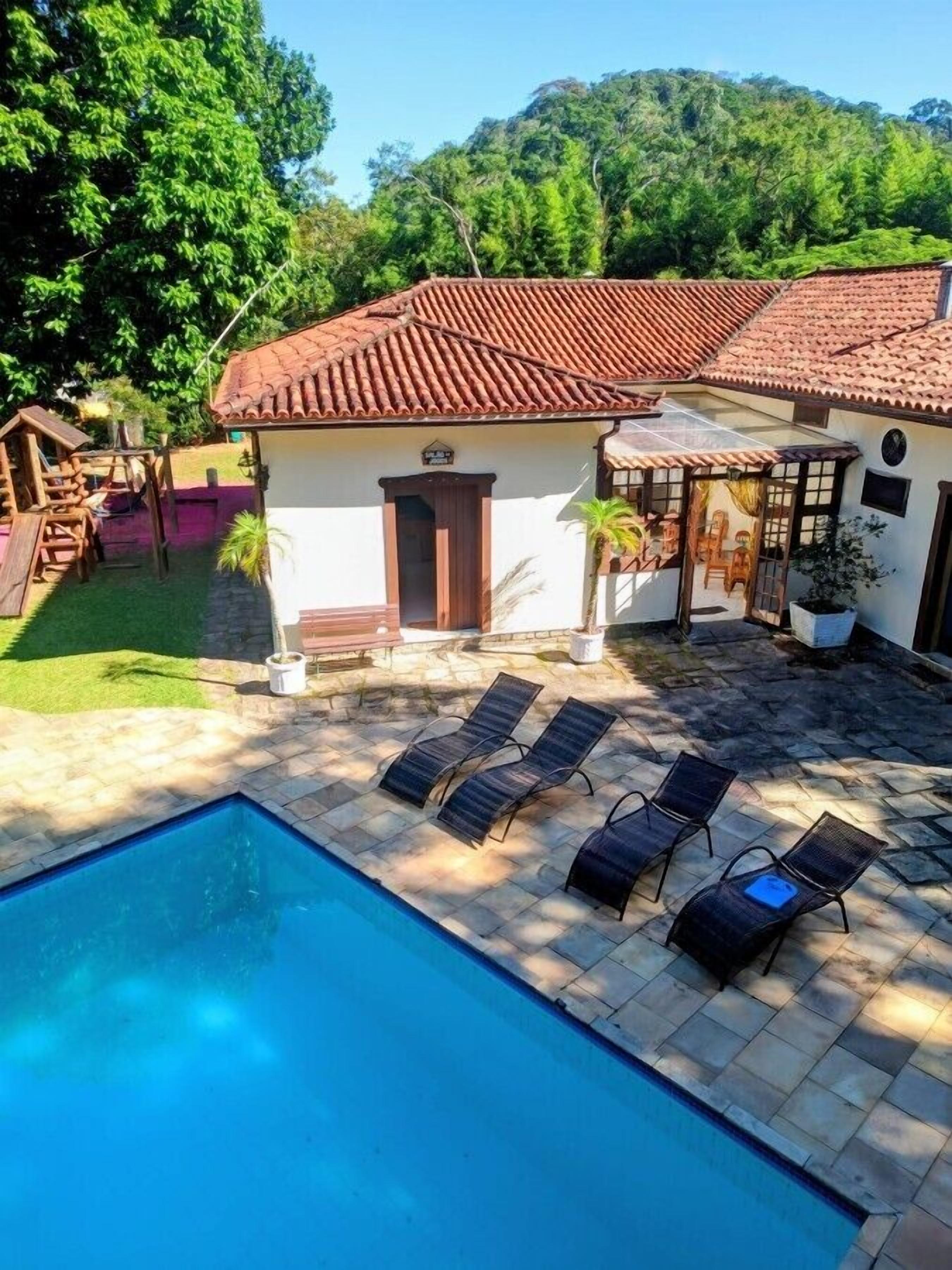 A pool with lounge chairs, a patio, and a building with a tiled roof.