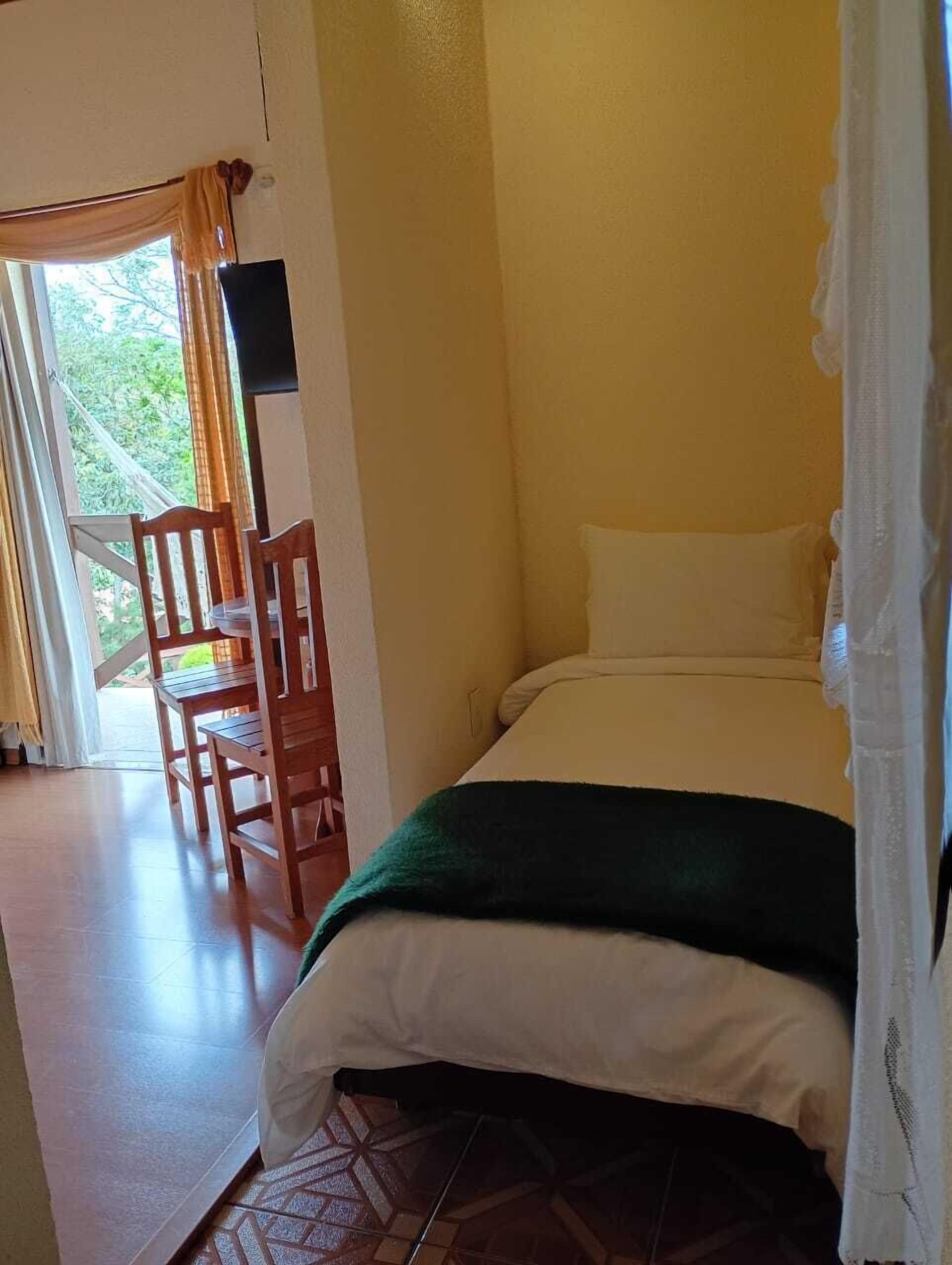 Una habitación con cama, una silla, una mesa y un ventanal con cortinas.