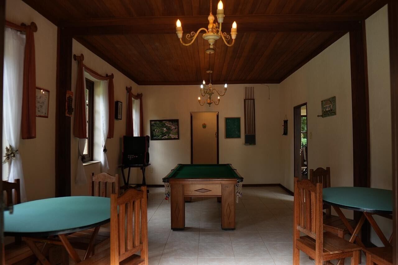 Um quarto com mesa de bilhar, cadeiras de madeira, um candelabro e quadros nas paredes.