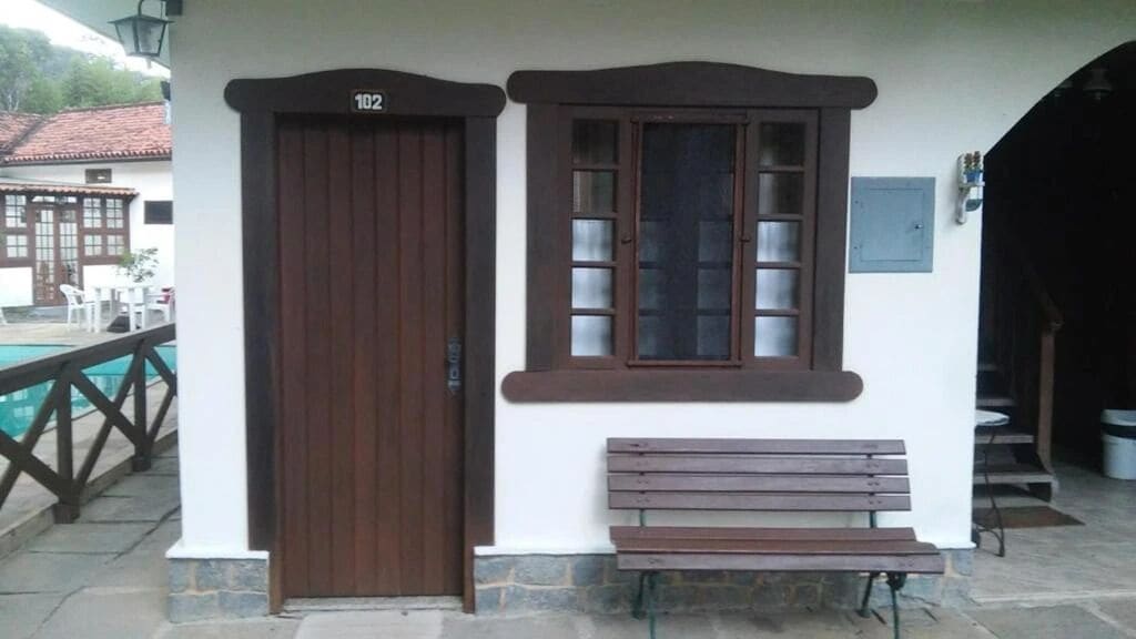 A building with a brown door marked "102", a window with multiple panes, and a bench outside.