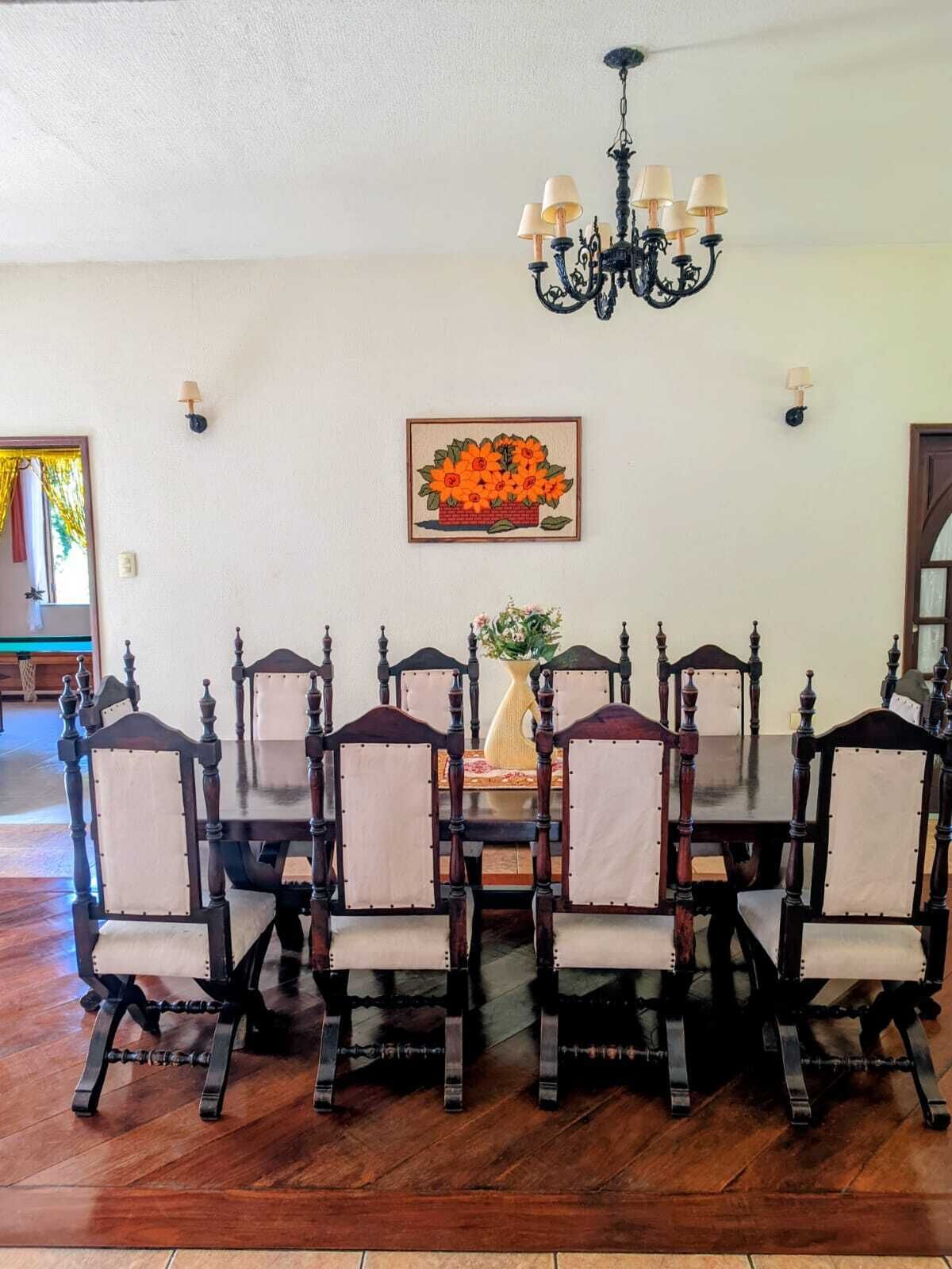 Comedor con una mesa redonda, seis sillas, una araña y una obra de arte floral enmarcada en la pared.