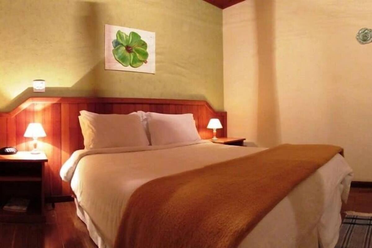 Ein Hotelzimmer mit einem Bett, zwei Nachttischlampen, einem Holz-Kopfteil, einem Wandbild und einem kleinen Tisch mit einer Lampe.