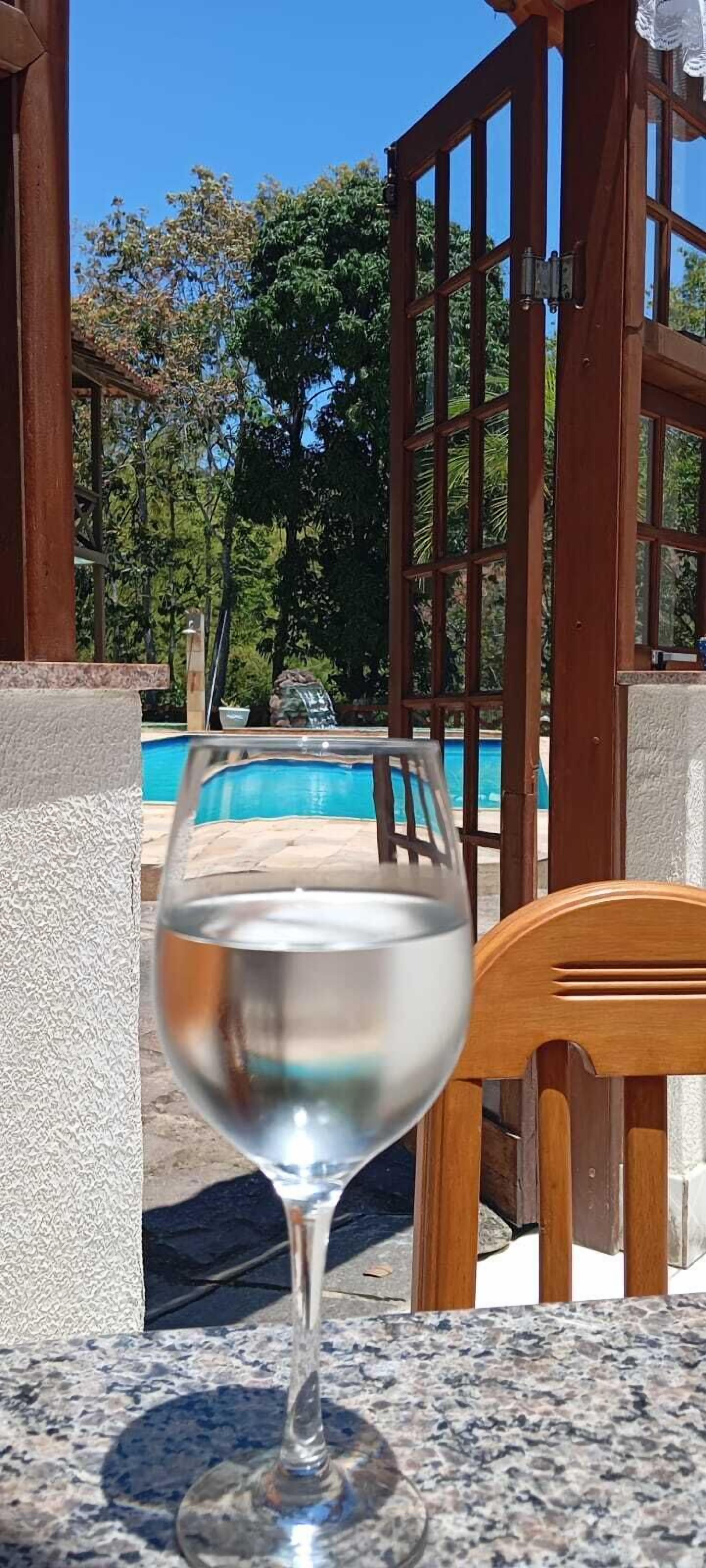 Un vaso de agua sobre una mesa, con una piscina al fondo.