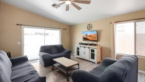 A living room with a ceiling fan, a flat-screen TV, and a kitchen area with cabinets. - 3 Bedrooms Near State Farm Stadium Pets (Phoenix)