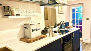 Een moderne keuken met donkere kastjes, een wit aanrechtblad en een ingebouwde oven. Op het aanrecht staat een broodtrommel met de tekst 'BREAD' en een koffiezetapparaat.