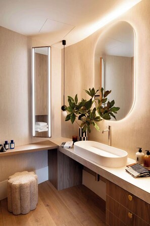 A modern bathroom with a large mirror, a wooden vanity, and a plant. - Stylish Apartment in Recoletos (Madrid)