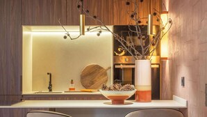 Una cocina moderna con pared de madera, encimera blanca, dos taburetes de bar y una lámpara colgante.