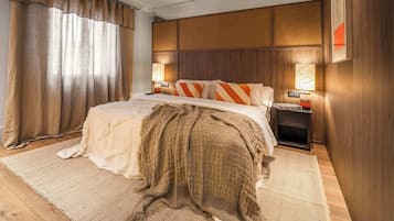 Een hotelkamer met een groot bed, houten hoofdeinde, twee bedlampen en een groot raam met gordijnen.