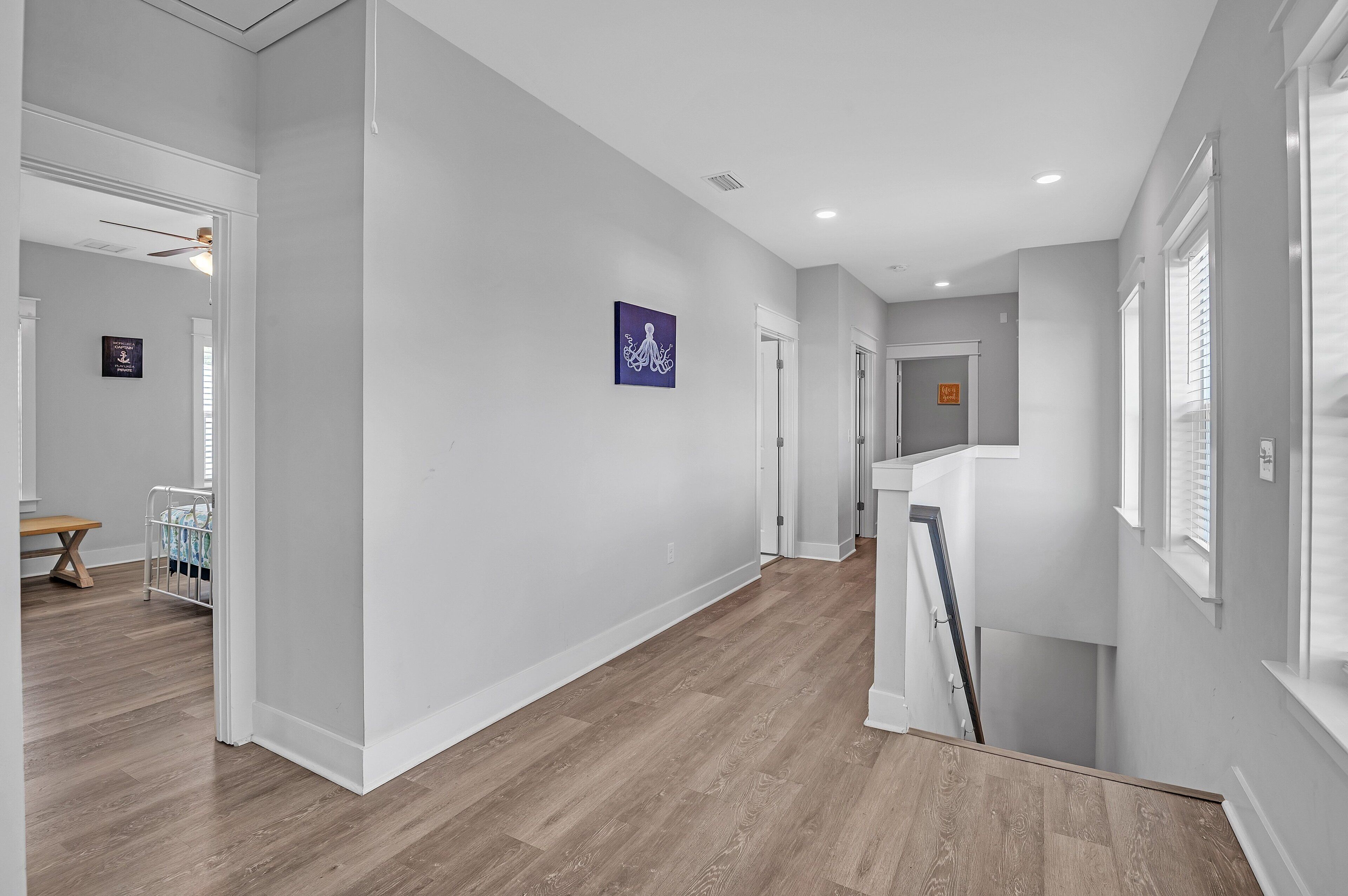 A spacious hallway with wooden flooring, white walls, and a ceiling fan.