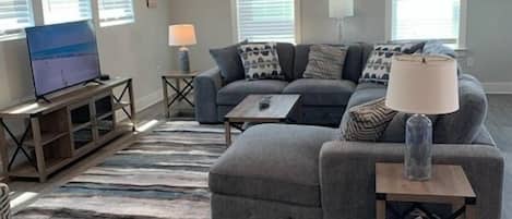 A modern living room with a grey sectional sofa, a flat-screen TV, and a ceiling fan.