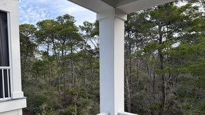 A white building with a balcony overlooking a forested area.