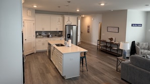 A modern kitchen with white cabinets, a central island, stainless steel appliances, pendant lighting, and a dining area with a table and chairs.