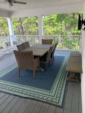 A covered outdoor patio with a table and chairs, surrounded by a white railing, and a view of greenery in the background. - Pet Friendly Beach Retreat on 30a - Sleeps 14 (Santa Rosa Beach)