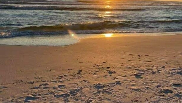 A beach with the sun setting over the ocean, creating a calm and serene atmosphere.