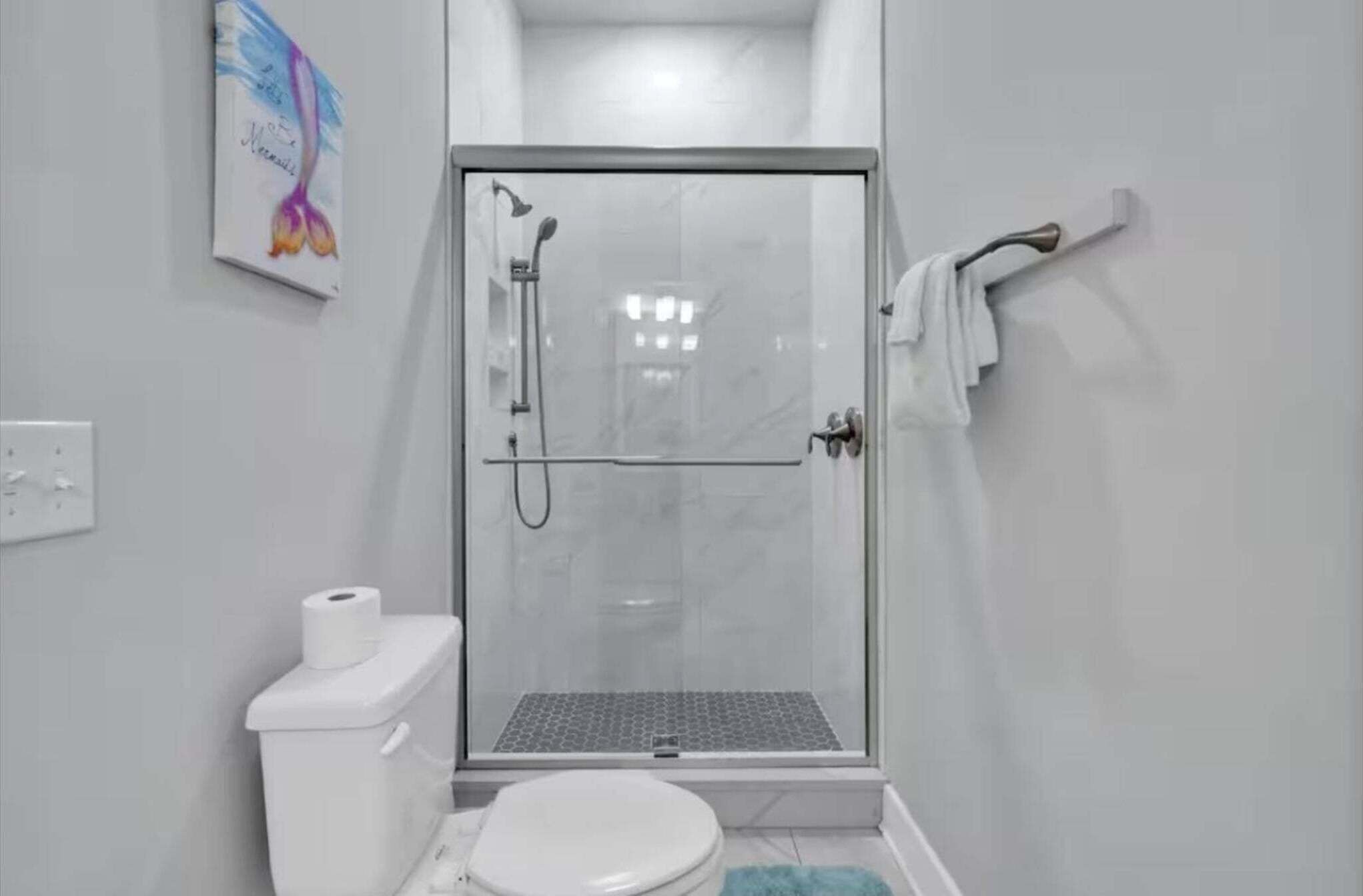 A small, modern bathroom with a glass shower enclosure, a toilet, and a towel rack.