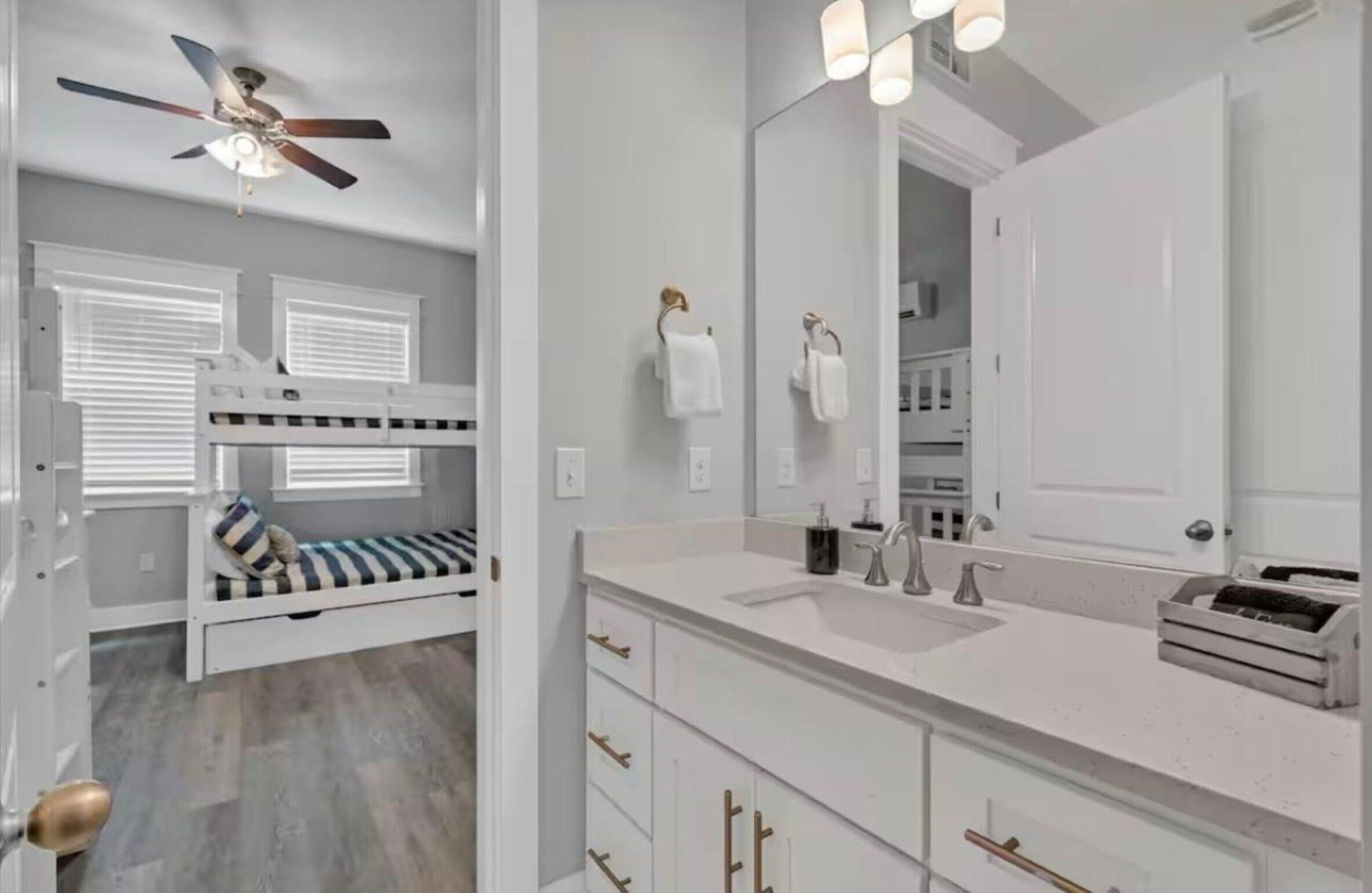 Ein Schlafzimmer mit Etagenbett, Deckenventilator, großem Spiegel und weißem Schminktisch mit Waschbecken.