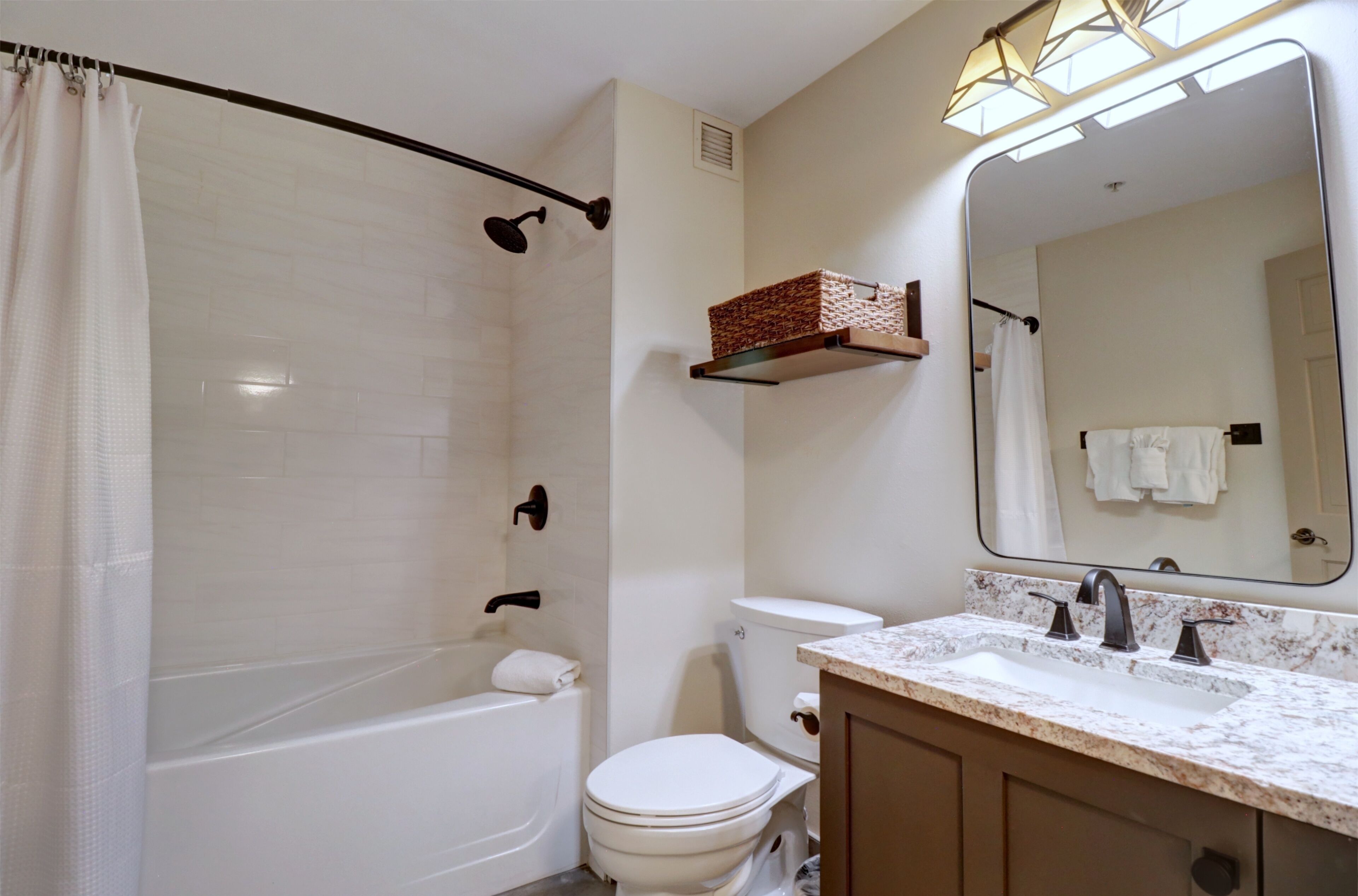 Un baño con bañera, inodoro y lavabo. Hay un estante sobre el lavabo y un espejo en la pared.