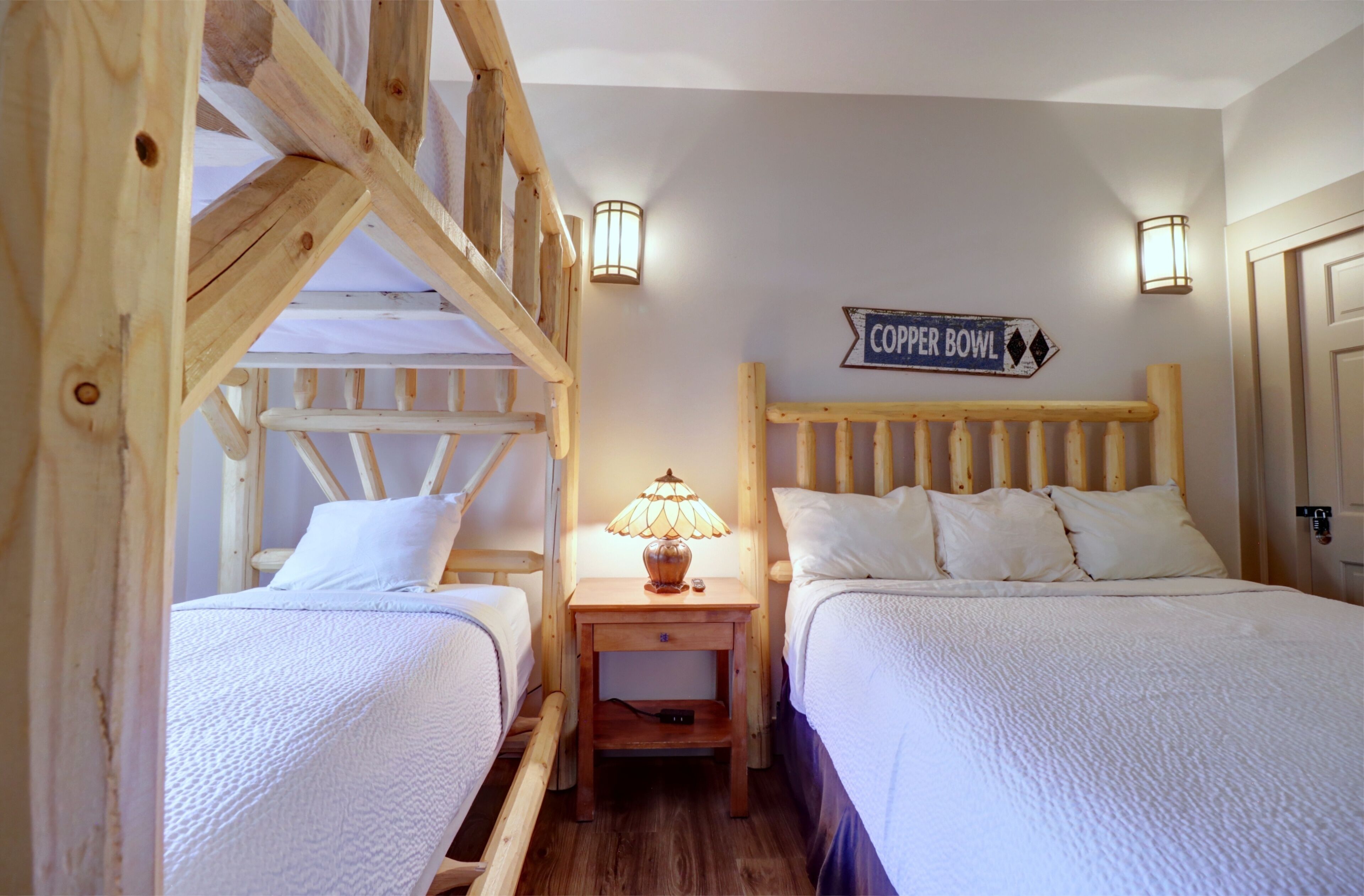 A cozy room with two wooden beds, a nightstand with a lamp, and a 'COPPER BOWL' sign on the wall.