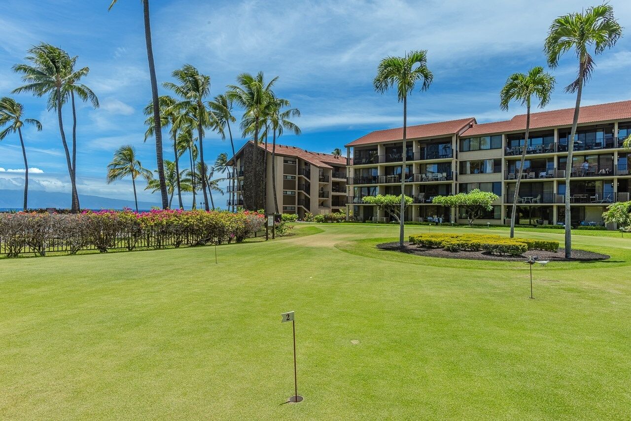 A golf course with a clubhouse, palm trees, and a clear sky.
