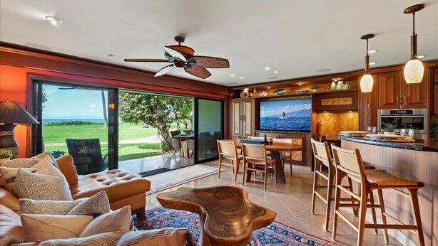 A modern living room with a large TV, a dining area, and a kitchen with bar seating. - Maalaea Surf C2 1 Bedroom Condo (Kihei)