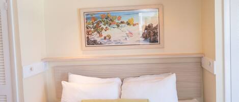 A bedroom with a bed, white pillows, a green pillow, a framed painting, and recessed ceiling lights.