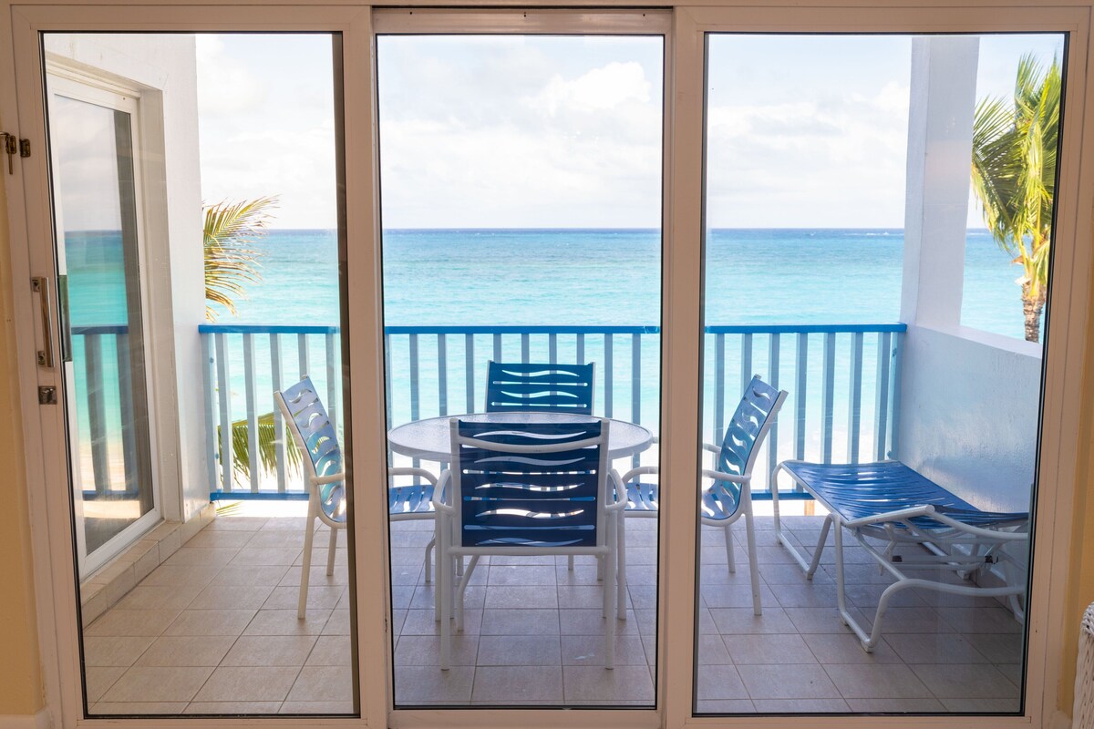A balcony with a table and chairs, a view of the ocean, and a palm tree.