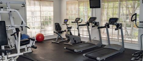 A gym with treadmills, elliptical machines, and a weight bench.
