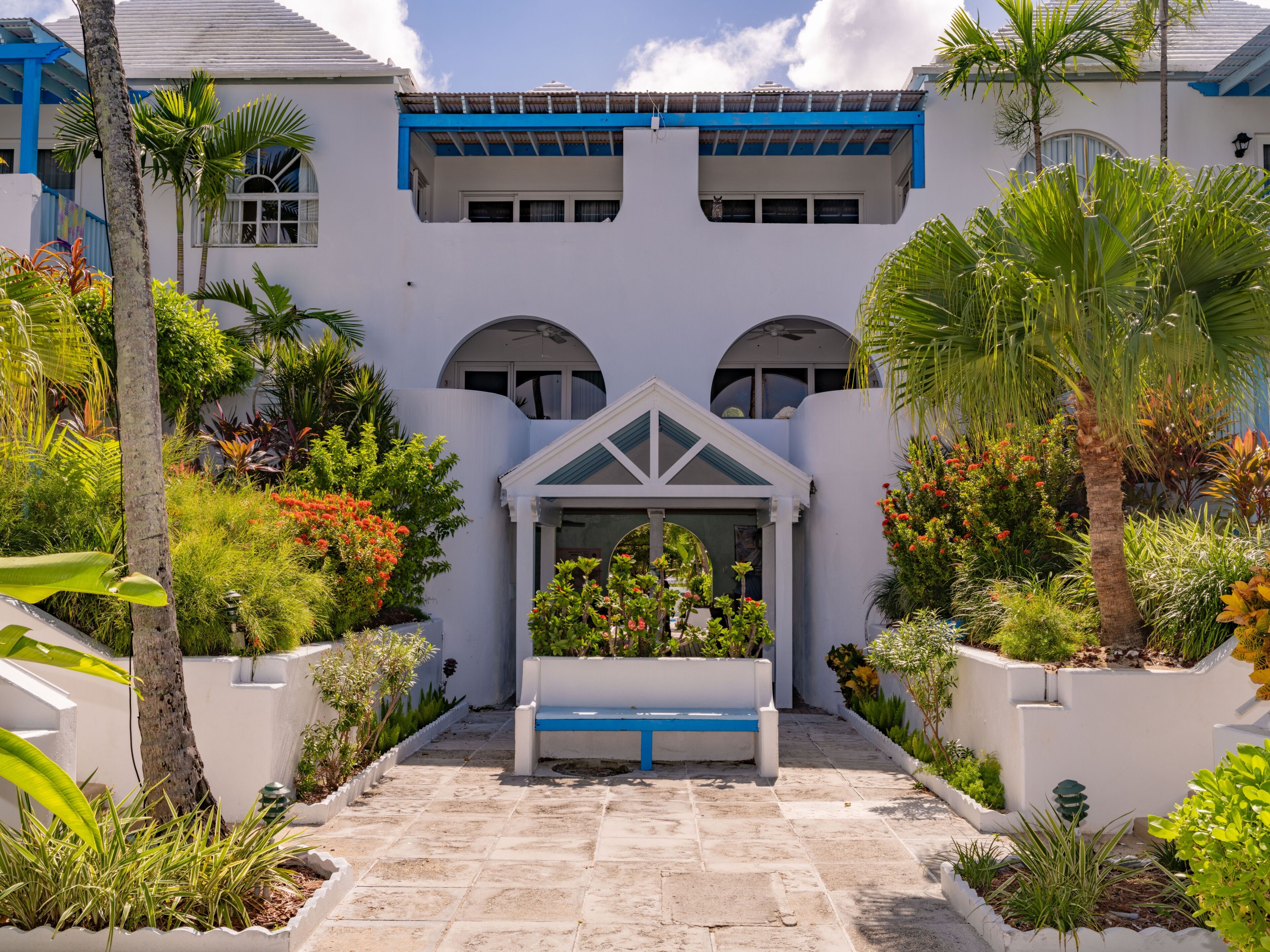 A white building with a blue roof, a central archway, and a bench in the courtyard.