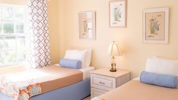 A hotel room with two beds, a nightstand with a lamp, and framed botanical illustrations on the wall.