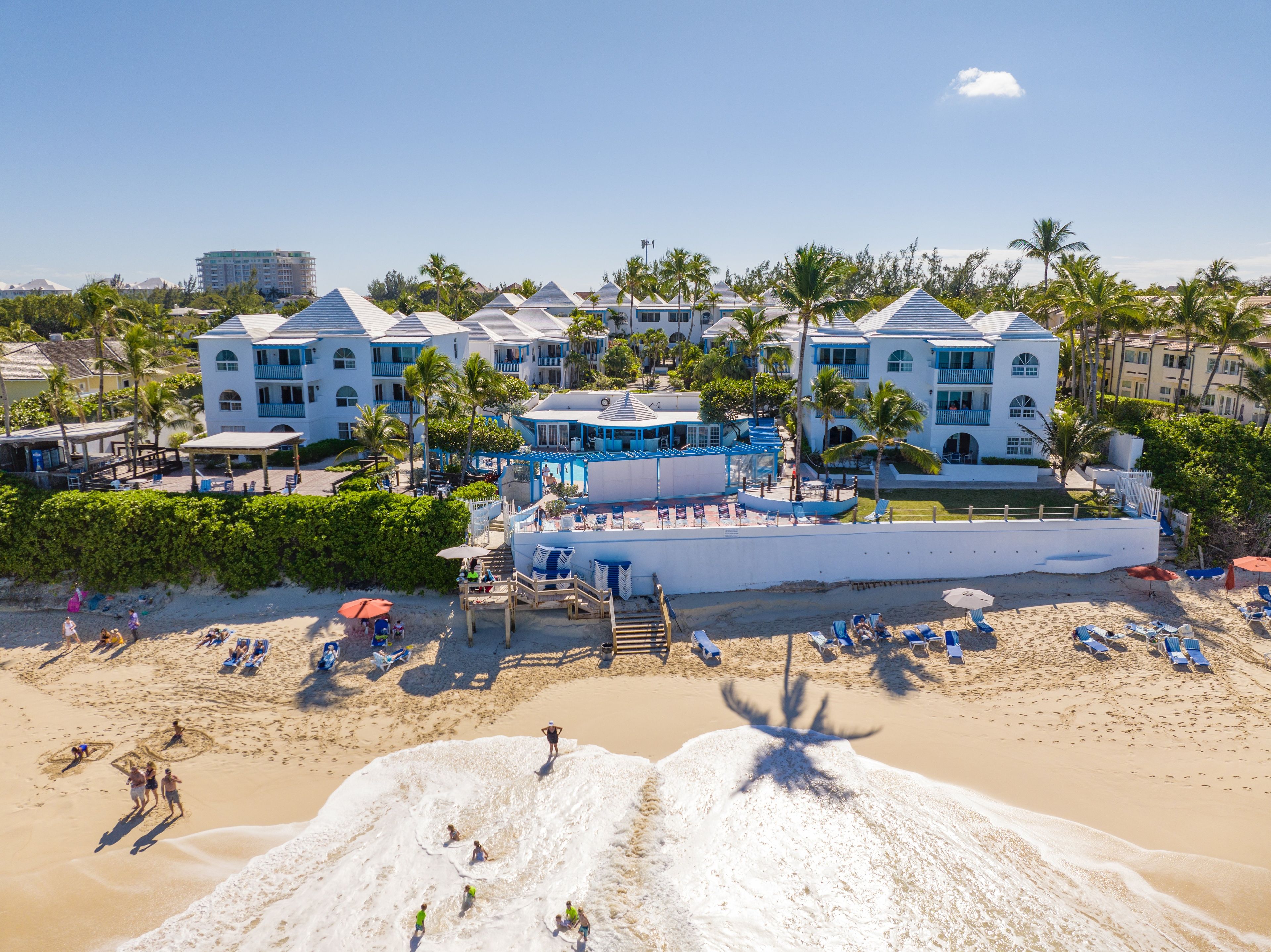 Un hotel frente a la playa con varias edificaciones, una playa de arena y palmeras.