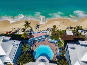 Luchtbeeld van een resort met een zwembad, strand en palmbomen.