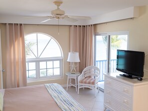 A bedroom with a bed, a television, a chair, a lamp, and a view of the outdoors.